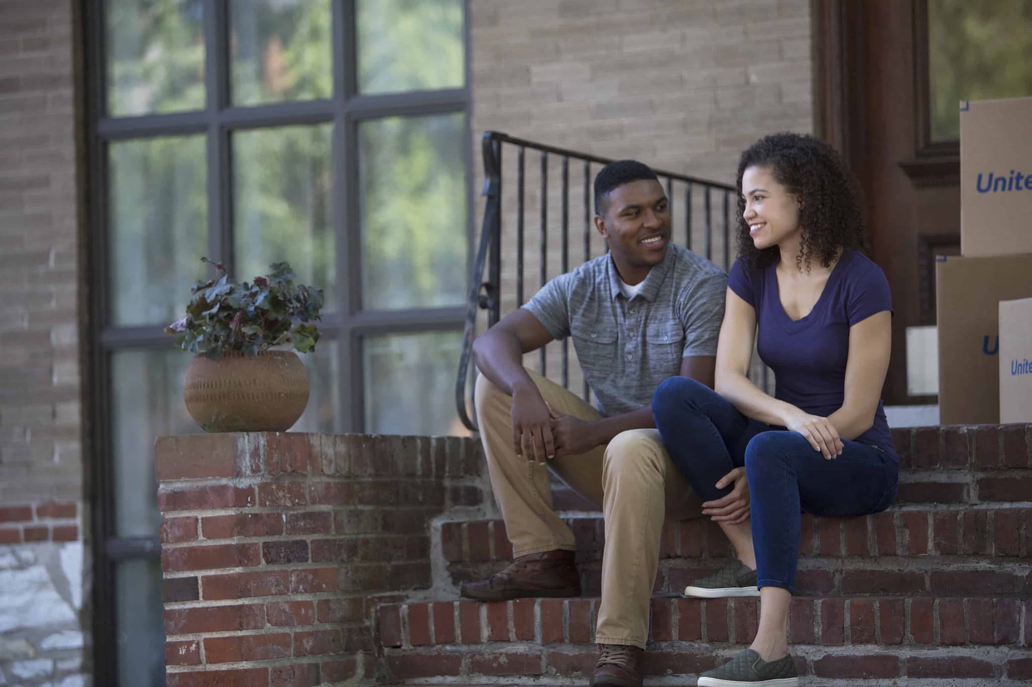 young couple sitting outside of their condo on the stairs with moving boxes beside them - United Van Lines®